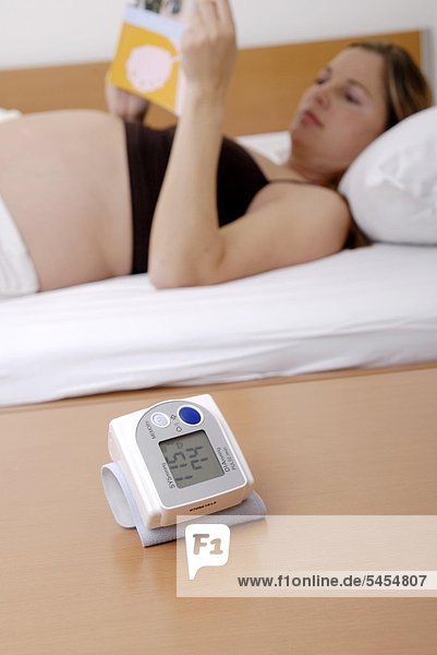 Schwangere nackte Frau liest mit Blutdruckmeßgerät