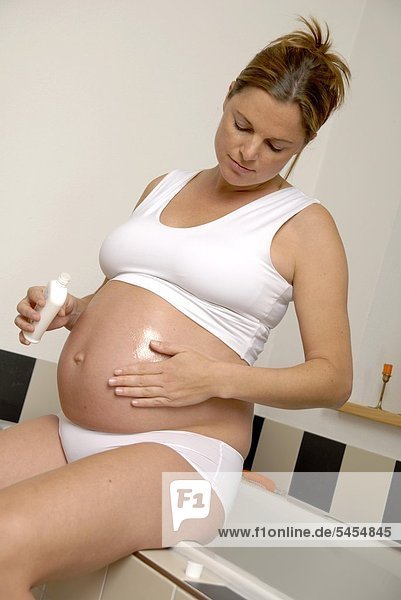 Schwangere Frau in Unterwäsche cremt sich den Bauch ein