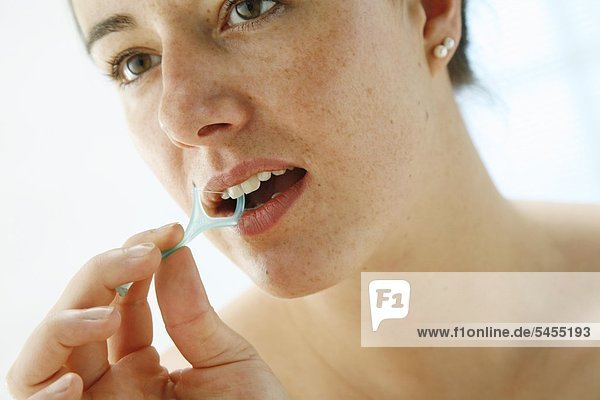 Portrait einer jungen Frau die sich die Zähne mit Zahnseide putzt