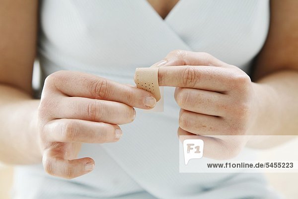 Nah Detail - junge Frau wickelt ein Pflaster um ihren Zeigefinger