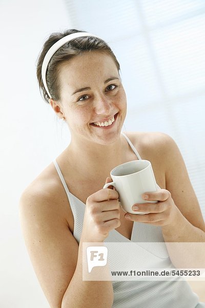 junge Frau hält eine Tasse mit Tee in den Händen und lächelt in die Kamera