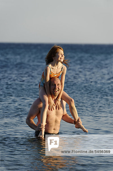 Vater trägt seine Tochter auf den Schultern  im Wasser im Meer