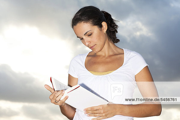 Frau liest Buch unter Wolkenhimmel