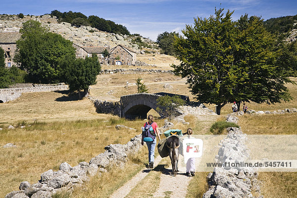 Mother and daughter walking with a donkey during a family-hike with a donkey in the Cevennes Mountains  France  Europe