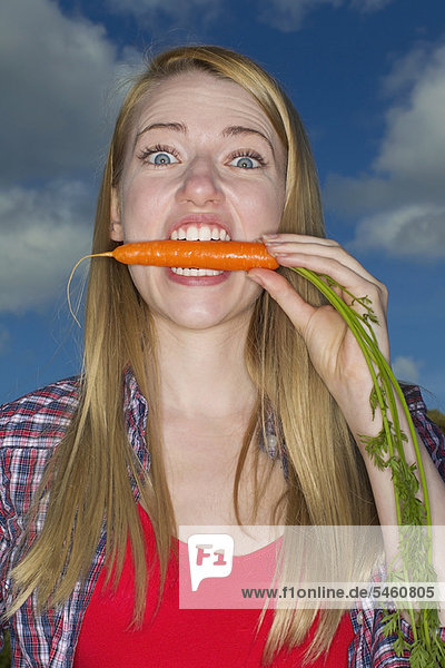 Frau beißt Karotte im Freien