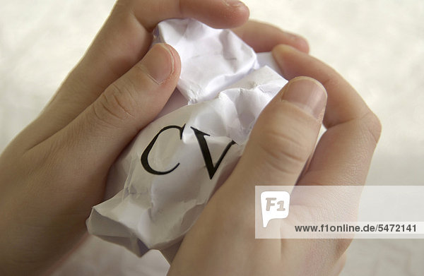 'Hand holding crumpled sheet of paper  ''CV'' for curriculum vitae written on it  symbolic image'
