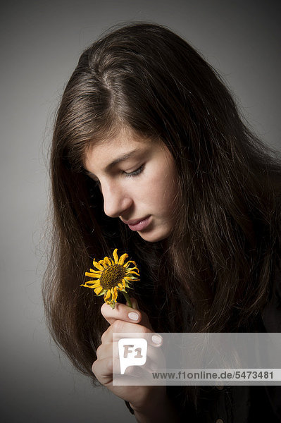 Mädchen  13 Jahre  schaut nachdenklich auf verwelkte Sonnenblume  Portrait