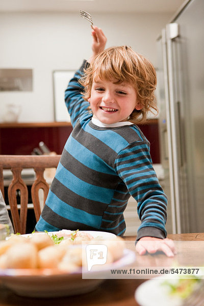 Young boy with fork raised about to stab potato