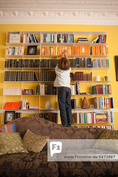 Young boy reaching up to get a book from a bookcase
