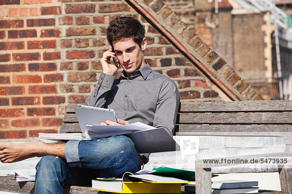 Junger Mann sitzt auf einer Bank mit digitalem Tablett und Handy