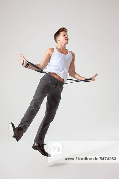 Young man in mid air pulling trouser braces