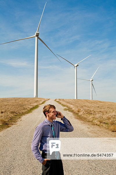 Man using mobile phone in front of wind turbines