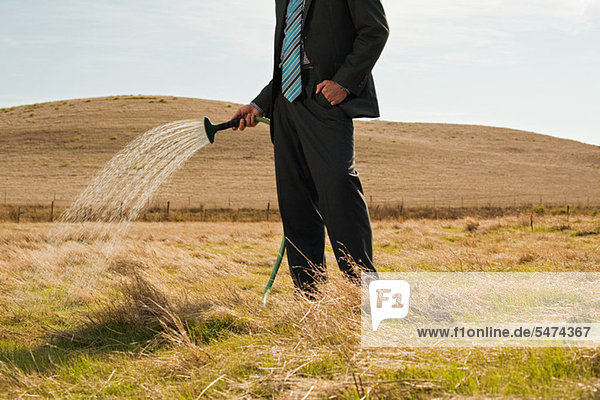 Mann spritzt Wasser auf trockenes Gras