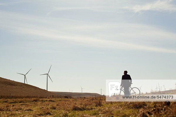Distant view of man by bicycle watching wind farm