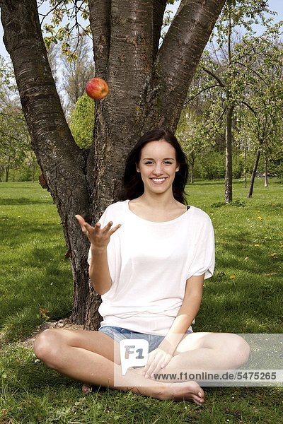 Junge Frau sitzt mit einem Apfel auf einer Wiese
