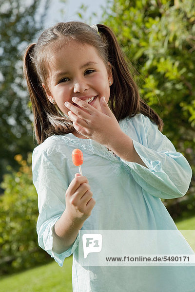 Girl holding lollipop in garden  smiling  portrait