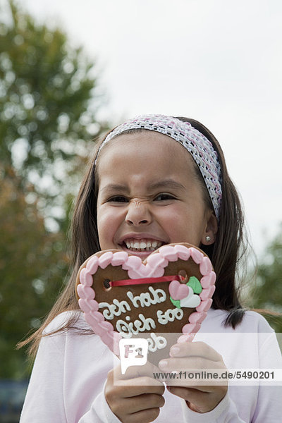 Mädchen hält Lebkuchenherz im Garten  lächelnd  Portrait