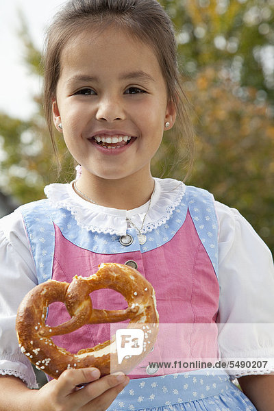 Girl holding pretzel in garden  smiling  portrait