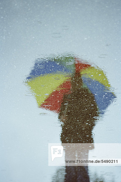 Junge Frau mit Regenschirm in Wasserpfütze reflektierend