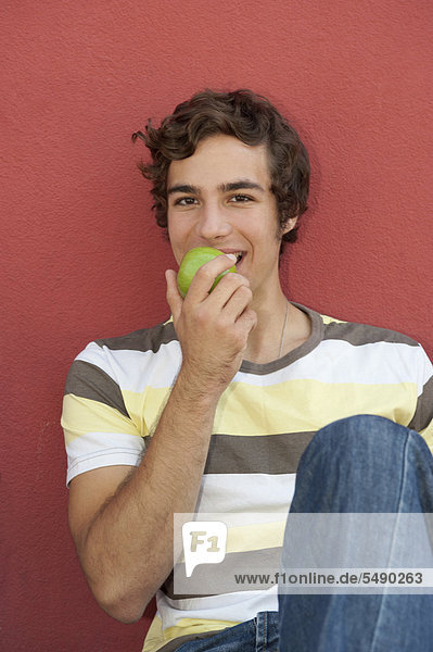 Junger Mann isst Apfel  lächelnd  Porträt