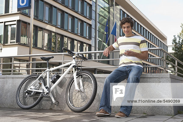 Junger Mann mit Fahrrad über Handy  lächelnd