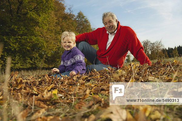 Deutschland  Bayern  Großvater und Enkelin sitzend Gras  lächelnd