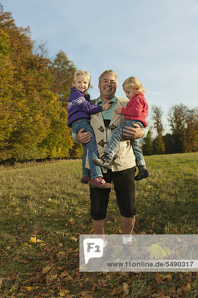 Deutschland  Bayern  Großvater mit Enkelinnen im Herbst  lächelnd