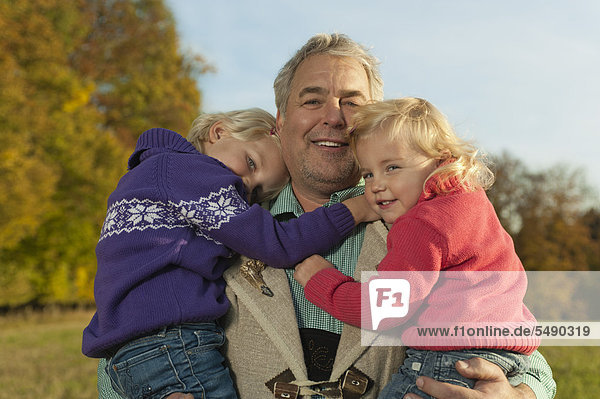 Deutschland  Bayern  Großvater mit Enkelinnen im Herbst  lächelnd