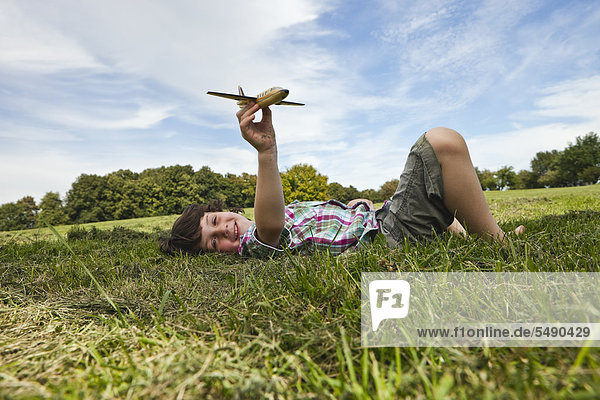 Junge spielt mit Modellflugzeug im Park  lächelnd  Portrait