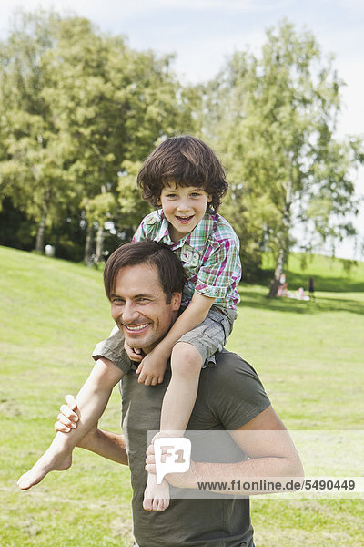 Deutschland  Bayern  Vater mit Sohn auf der Schulter im Park  lächelnd
