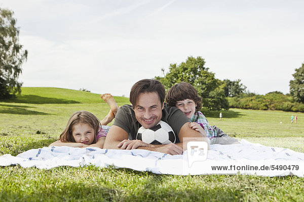 Deutschland  Bayern  Familie auf Decke im Park liegend  lächelnd  Portrait