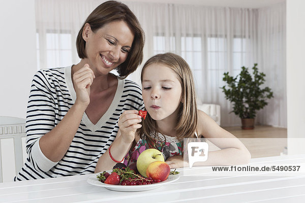 Deutschland  München  Mutter und Tochter essen Früchte  lächeln