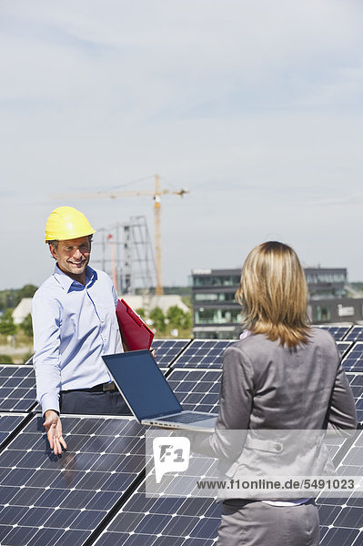 Germany  Munich  Engineers with laptop and discussing in solar plant