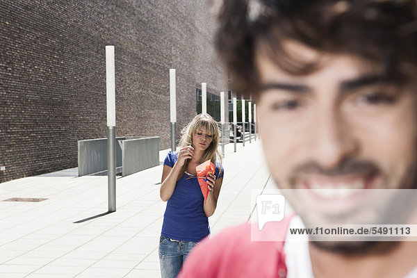 Junger Mann lächelt  Frau isst Pommes frites im Hintergrund