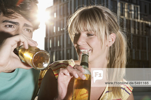 Deutschland  Köln  Junges Paar trinkt Bierflasche  lächelnd