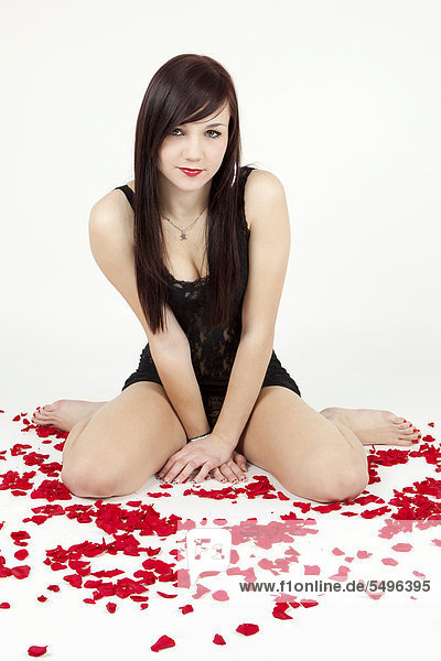 Young woman wearing black lingerie sitting between rose petals