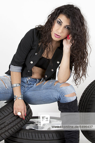 Junge Frau posiert mit kurzer Jacke  Jeans und Stiefeln auf Autorädern