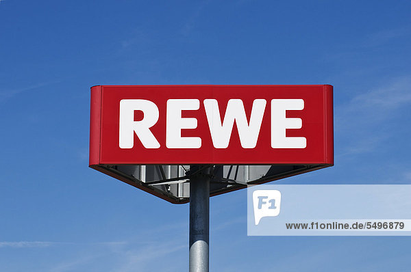 Logo  Schild des Supermarktes REWE vor blauem Himmel
