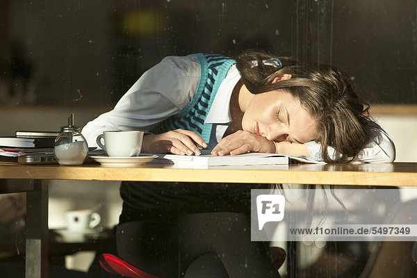 Student sitting in a cafe  she has fallen asleep over her notes  seen through a window