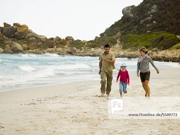 Parents running on the beach with their daughter.