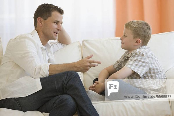 Vater im Gespräch mit Sohn auf sofa