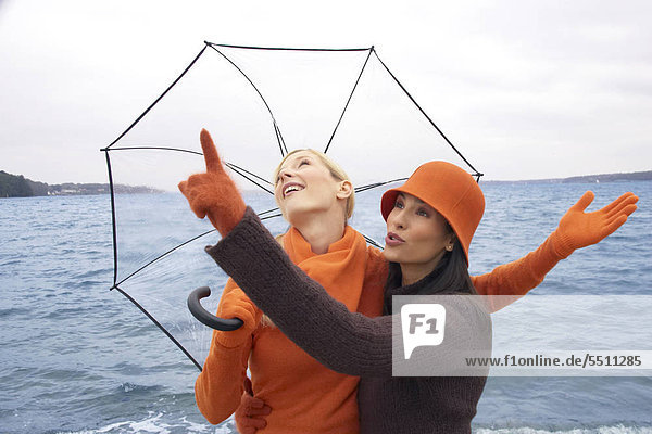Zwei junge Frauen mit Regenschirm am Meer Zwei junge Frauen mit Regenschirm am Meer