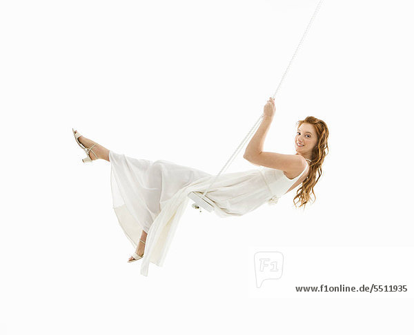 Caucasian bride swinging in swing set and looking at viewer.