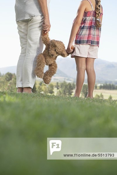 Grandmother and granddaughter holding teddy bear in rural field