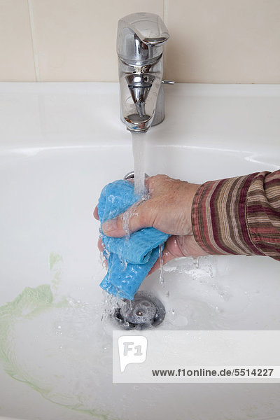 Waschbecken wird gereinigt  laufender Wasserhahn  Hand wäscht Schwammtuch aus