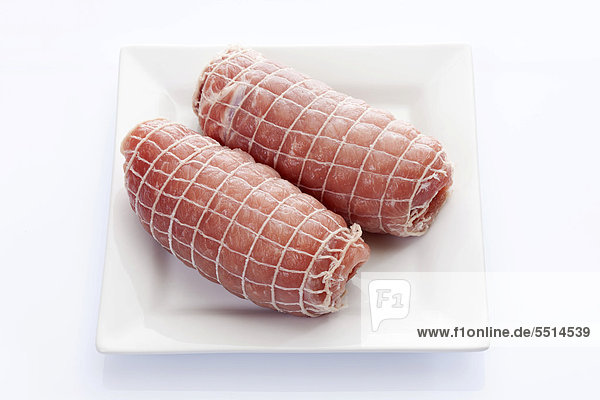 Rohe Schweinefleisch-Rouladen mit Netz auf Porzellanteller