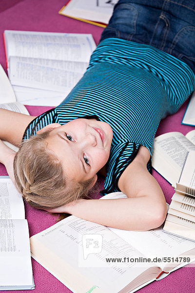8-jähriges Mädchen liegend zwischen Büchern