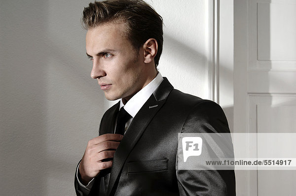 Modeaufnahme  junger Mann im Anzug richtet Krawatte