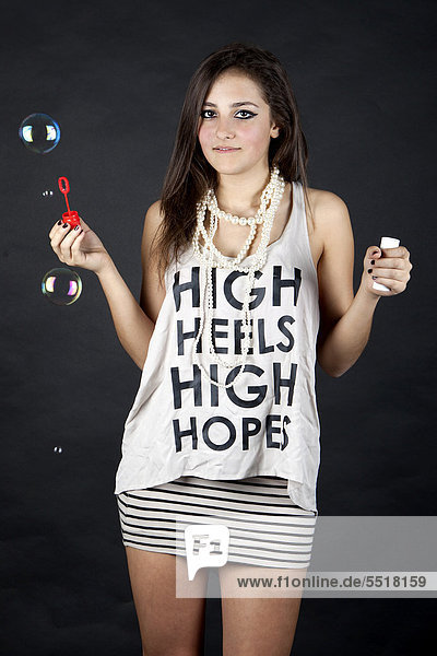 Junge Frau mit Seifenblasen und Top mit der Aufschrift High heels  high hopes