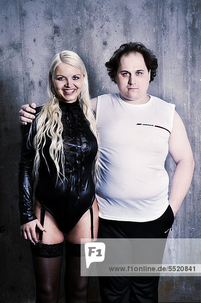 Blonde slim young woman wearing black lingerie and garter belts  standing arm in arm with an overweight man